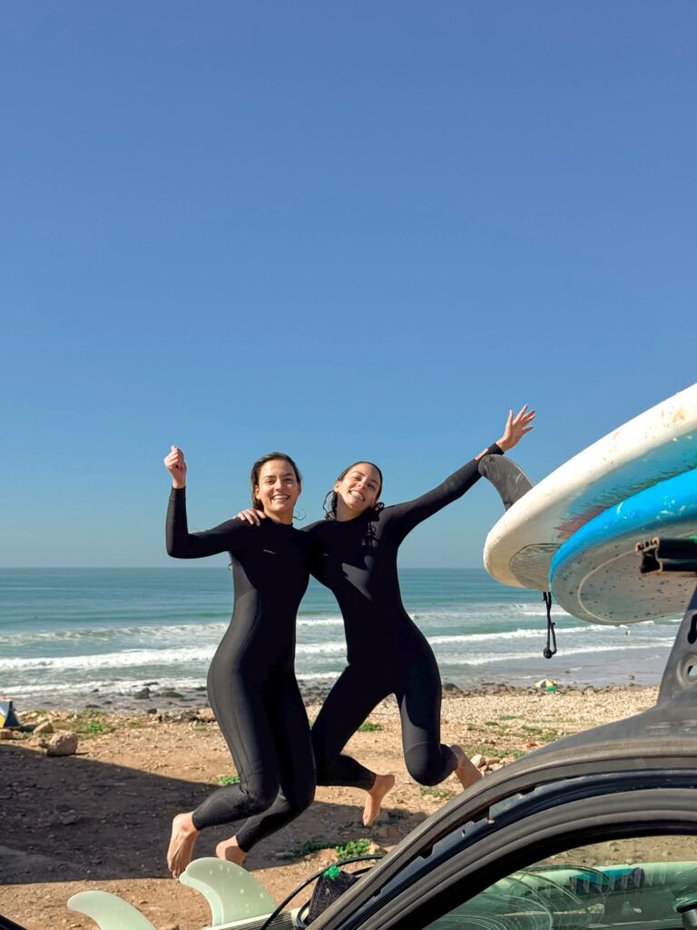 Two surfers jumping with joy on the beach after a surf session